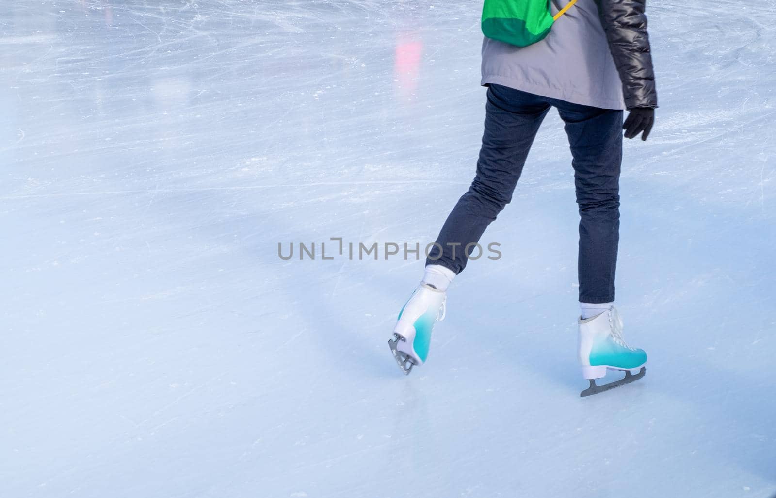 A young girl skating in winter clothes for outdoor activities at the rink in winter. Healthy lifestyle, active rest. Horizontal orientation, selective focus.