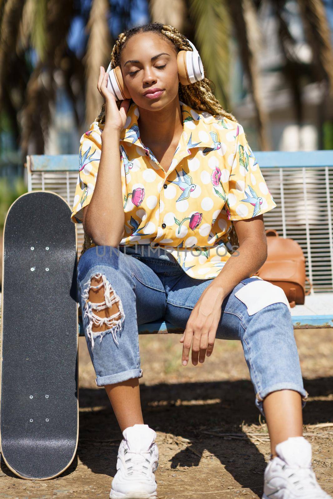 Young smiling African woman with skateboard Mixed-race girl relaxing after riding skateboard listening to the music outdoors.