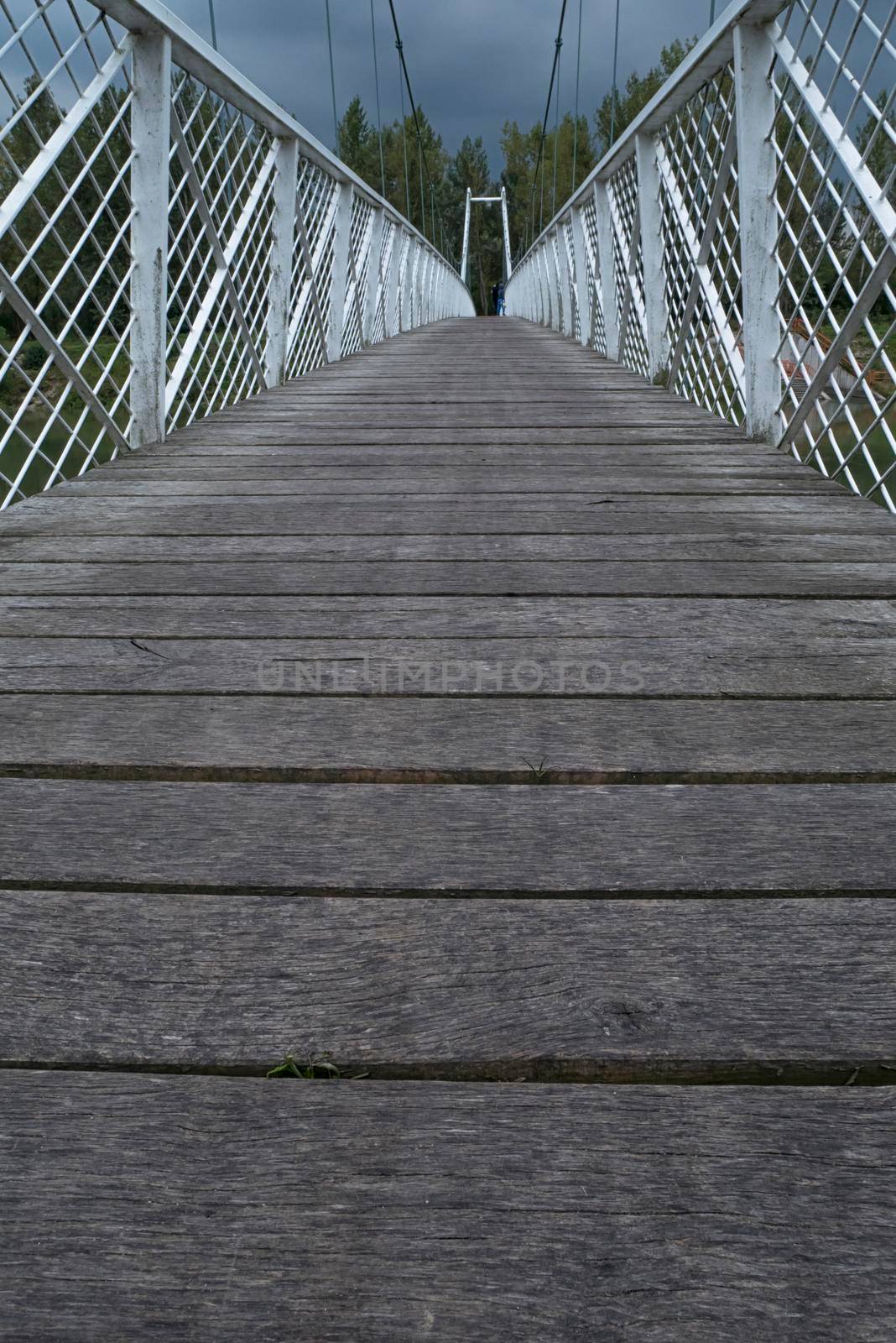 Low view of the bridge. Wood paved and white fence bounded by a suspension bridge in the Donja Dubrava. The bridge is the last building at the Donja Dubrava hydroelectric power plant. The gloomy weather and low view seem to be the starting point of a long journey.