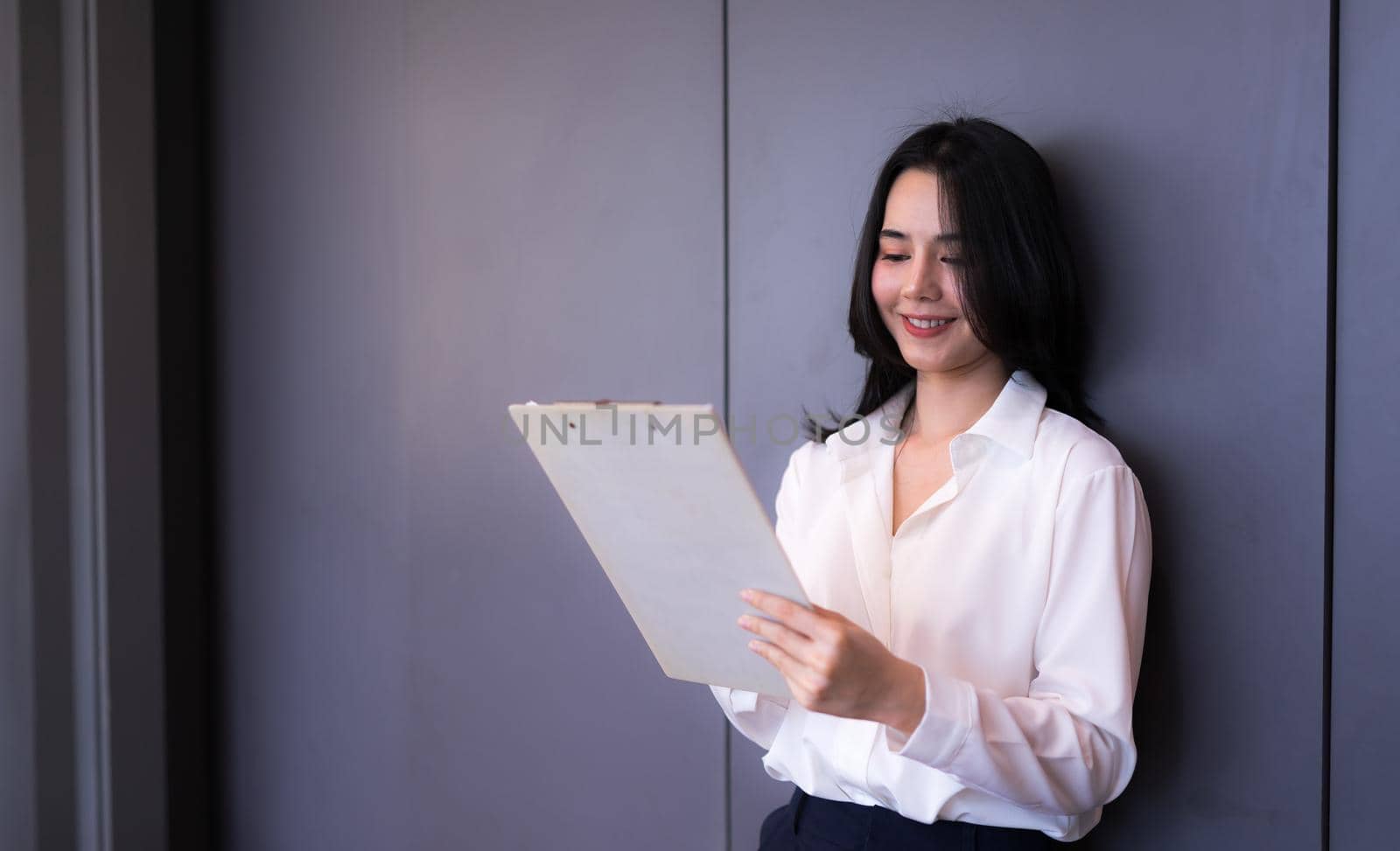 Asian young business female smailing and reading company earnings report in modern office.