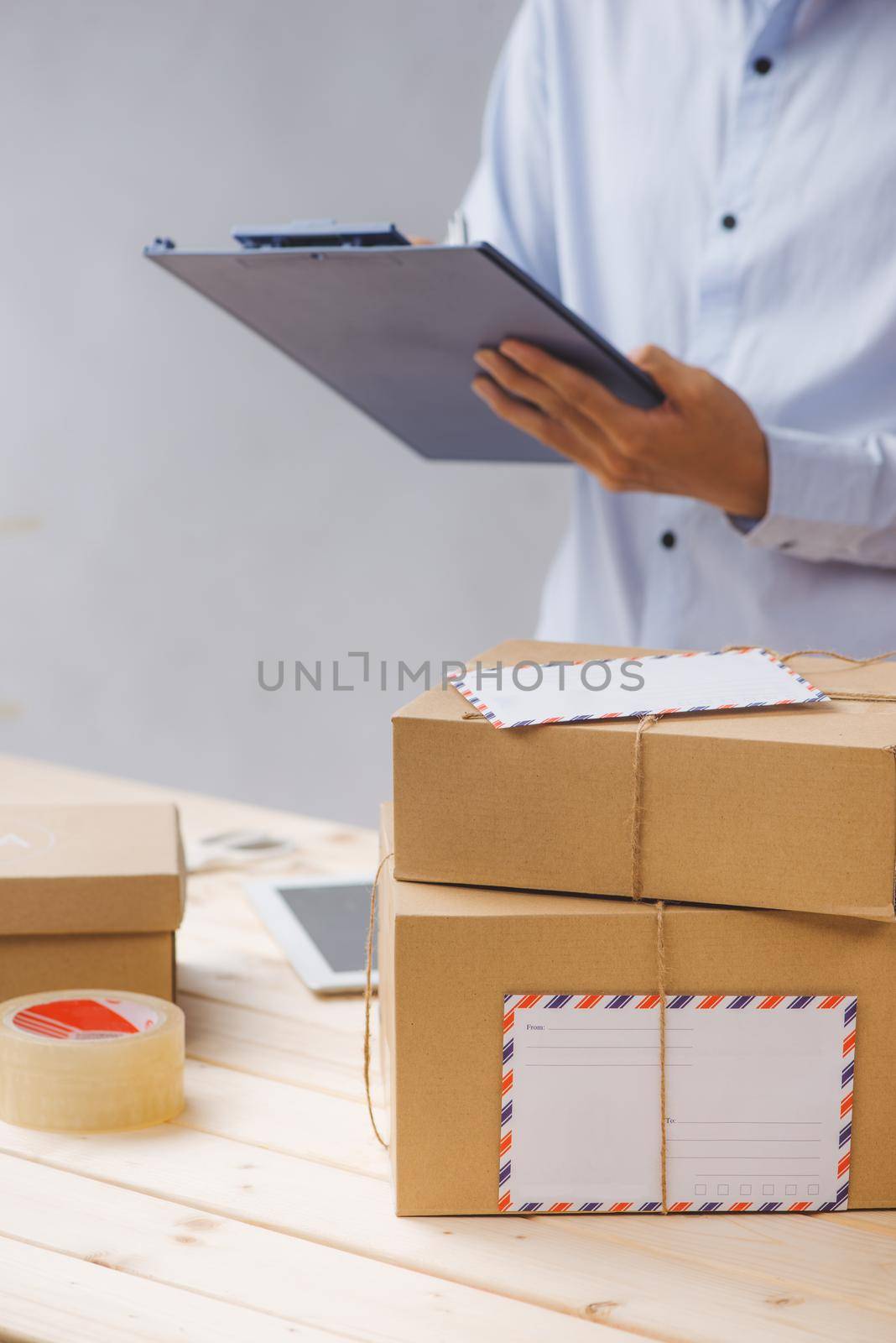 Courier making notes in delivery receipt among parcels at table