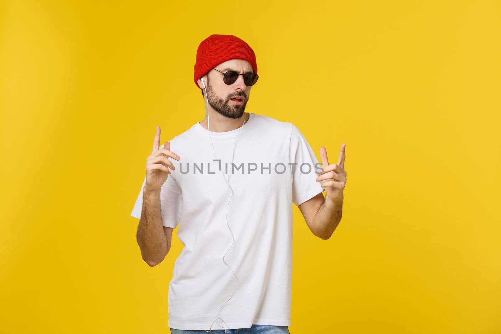 Portrait of a handsome young man dancing and listening music, isolated on yellow background.