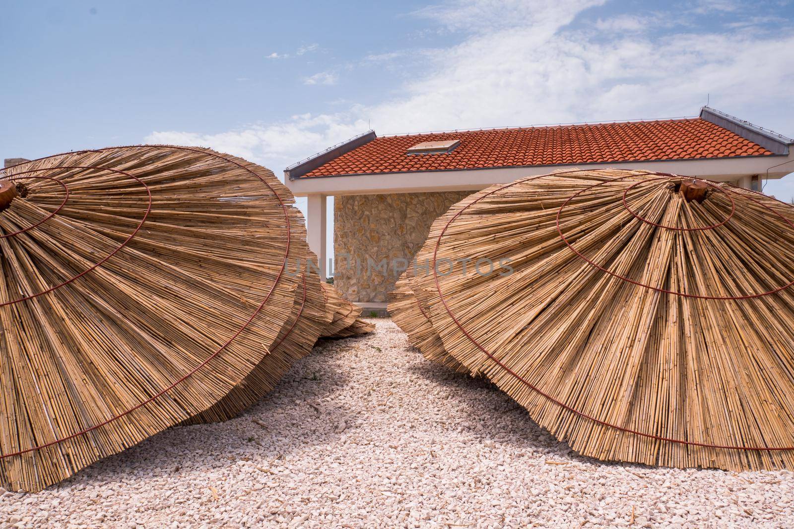 Lot of straw beach umbrellas laying down. Made of straw, wood and iron rings.