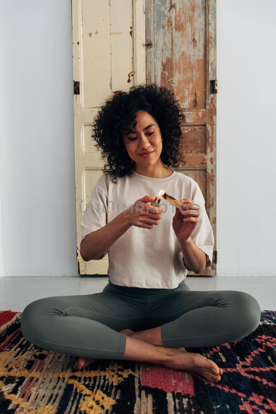 Young multiracial woman lighting palo santo at home prepares to meditate. Vertical image. by Hoverstock