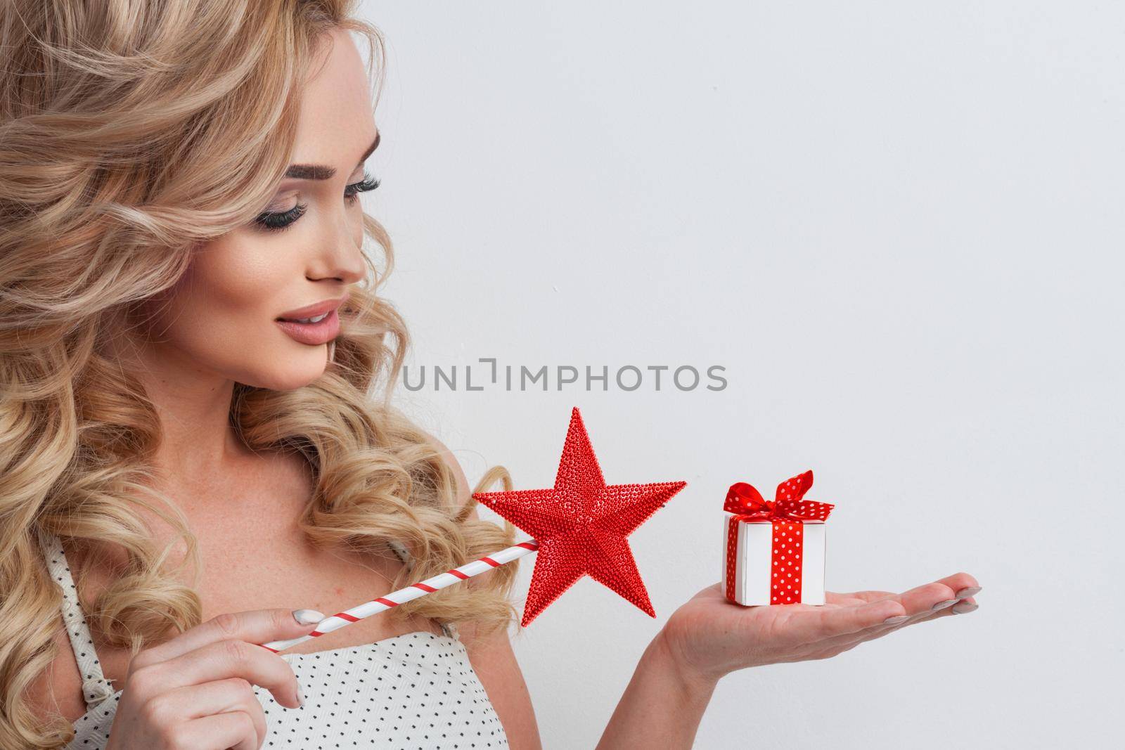 Portrait of a girl dressed in white dress holding magic wand and a present box over white background