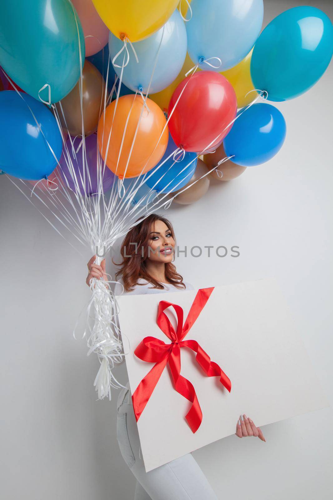 Young smiling woman with many colorful balloons and big gift box