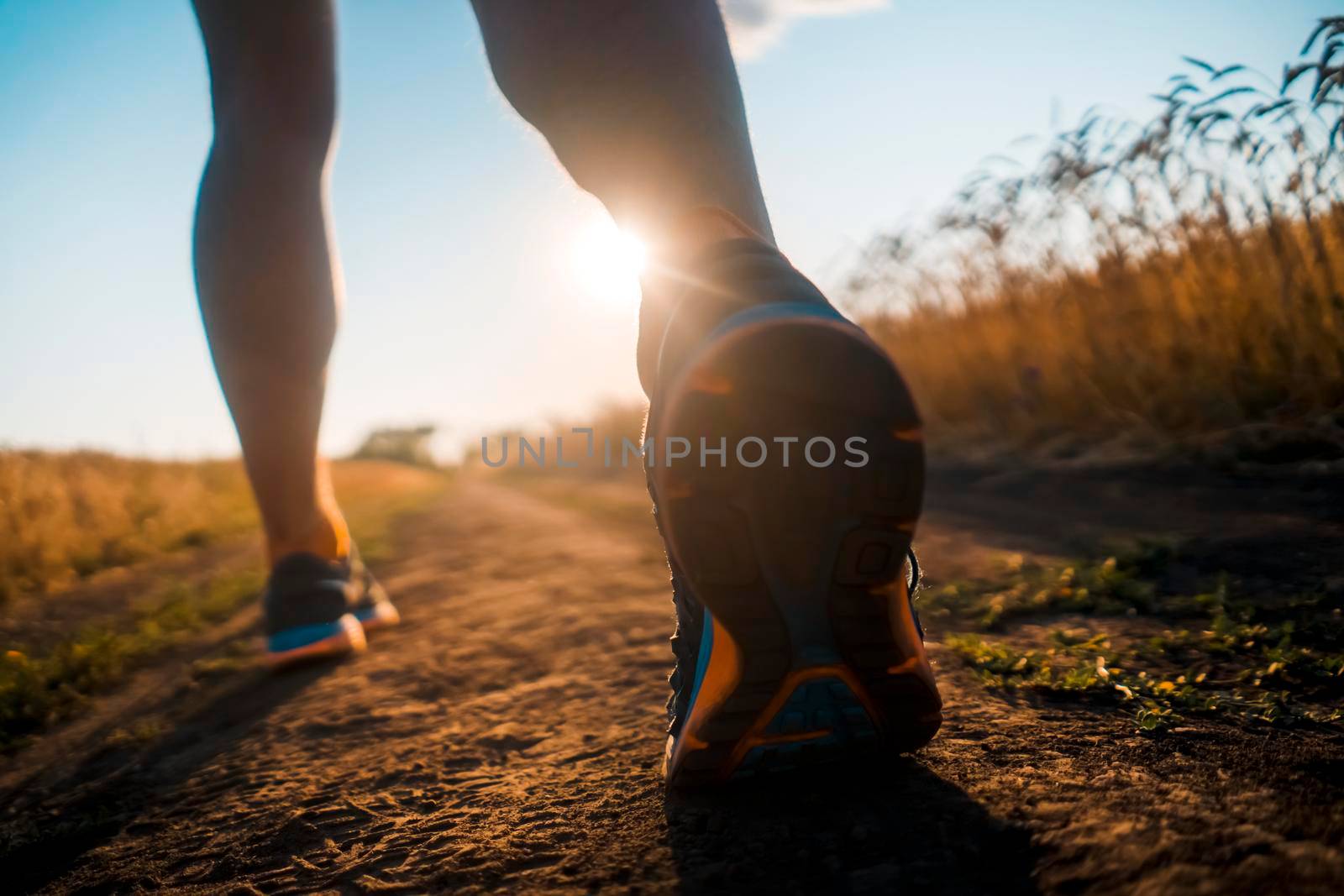 Athlete runner legs running on a close-up of a trail across a field on a shoe. Fitness and warm-up, young man with sun effect in the background and open space around him.