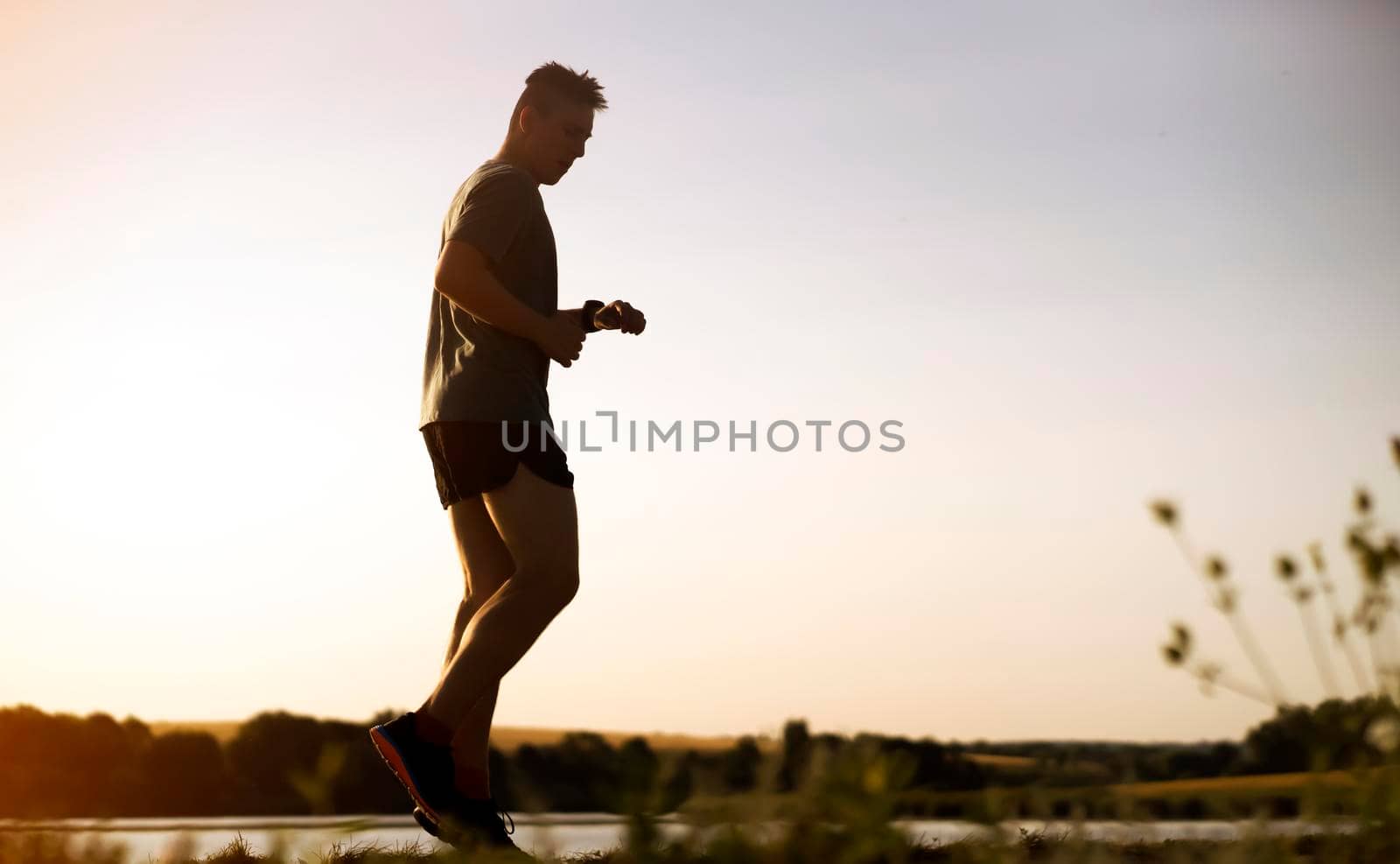 Young man doing cardio workout, exercising and running early in the morning at dawn near a beautiful lake. The athlete is preparing for the marathon.