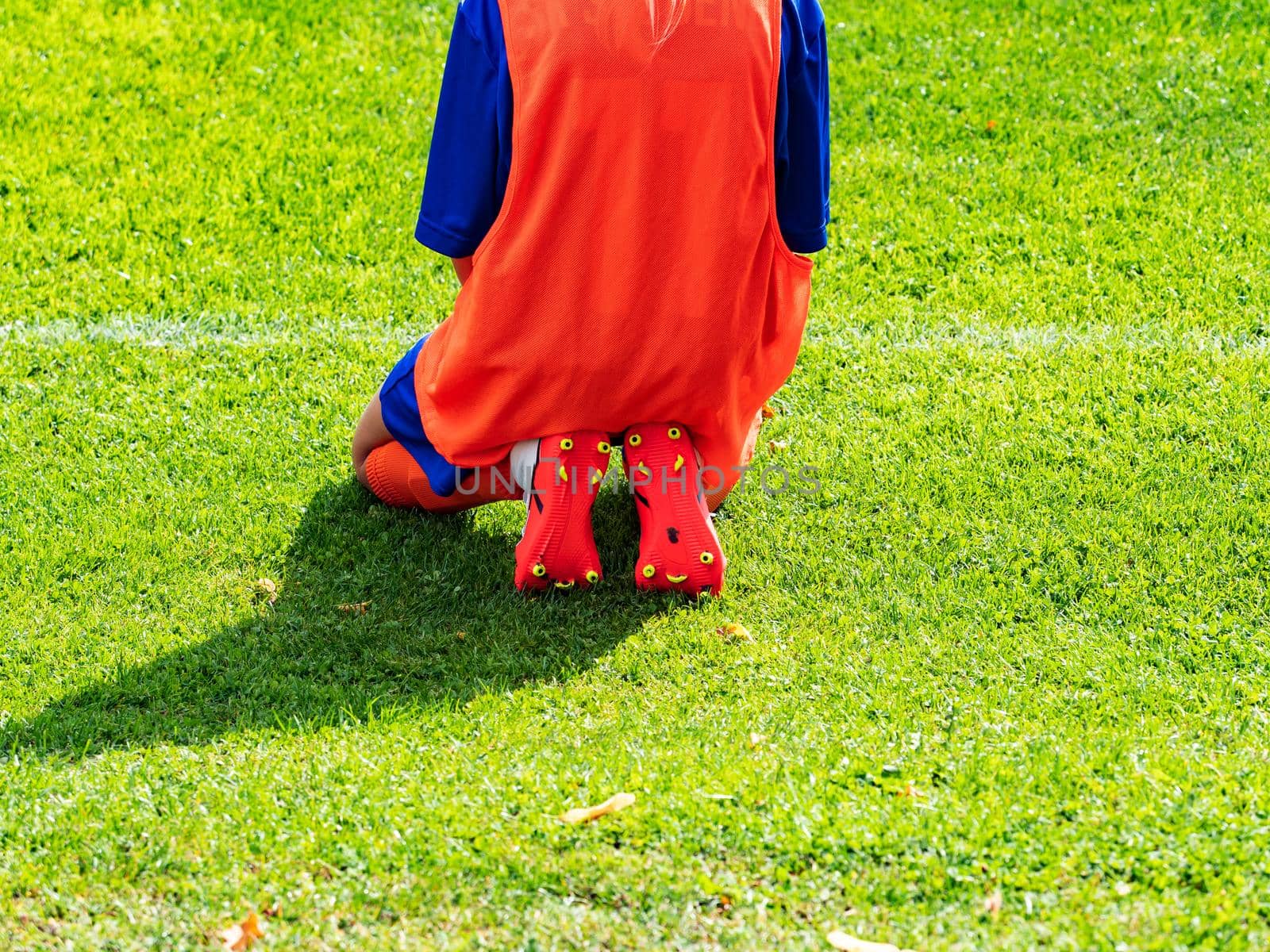 Girl in red sportive jersey and sneakers sitting at football playfield.  by rdonar2
