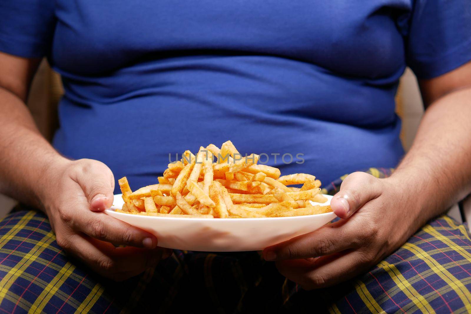 a fat man eating french fries while sited .