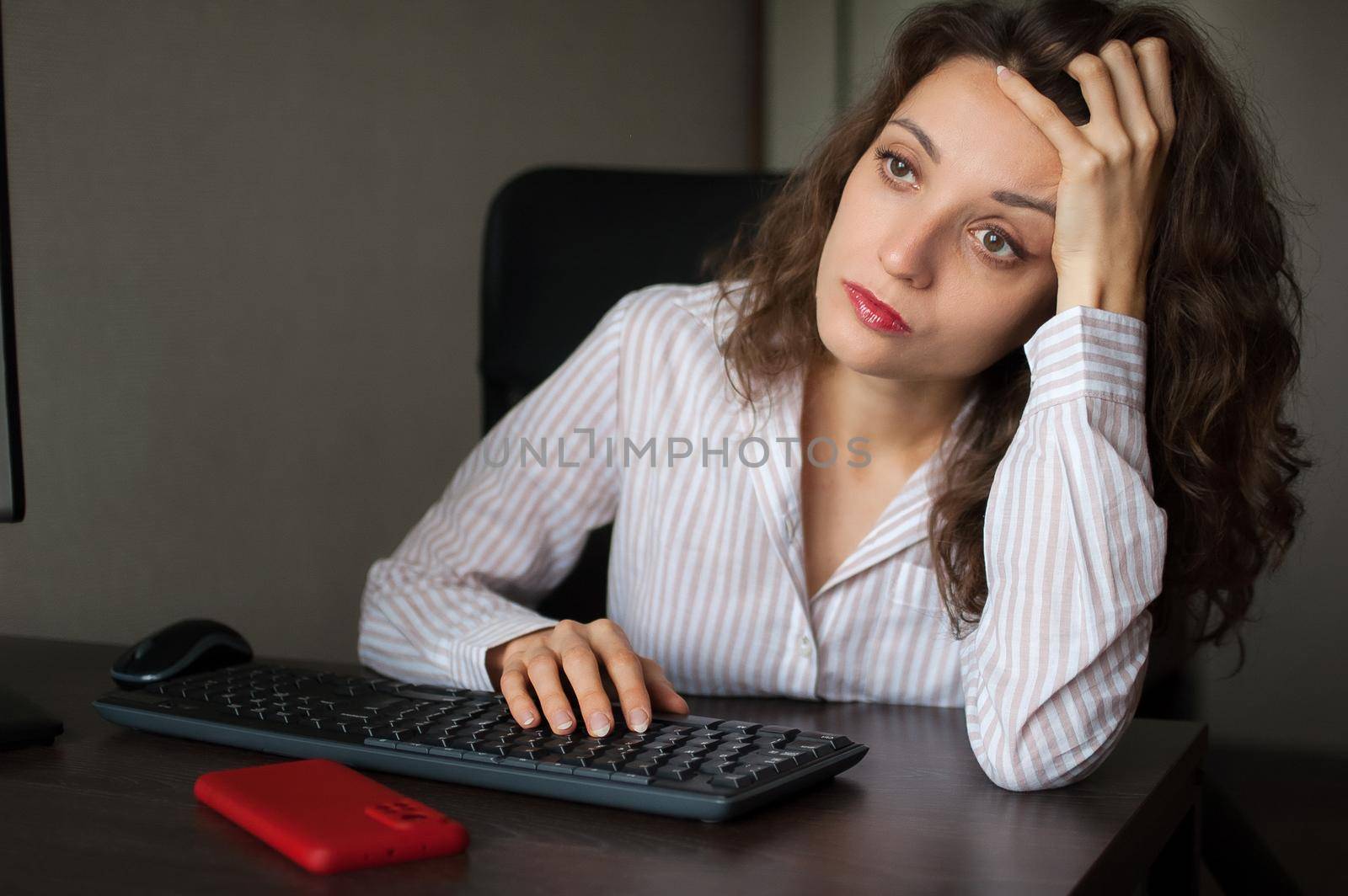 Tired young woman with curly hair and white shirt is working at the office using her laptop, routine work, freelance, burnout syndrome by balinska_lv