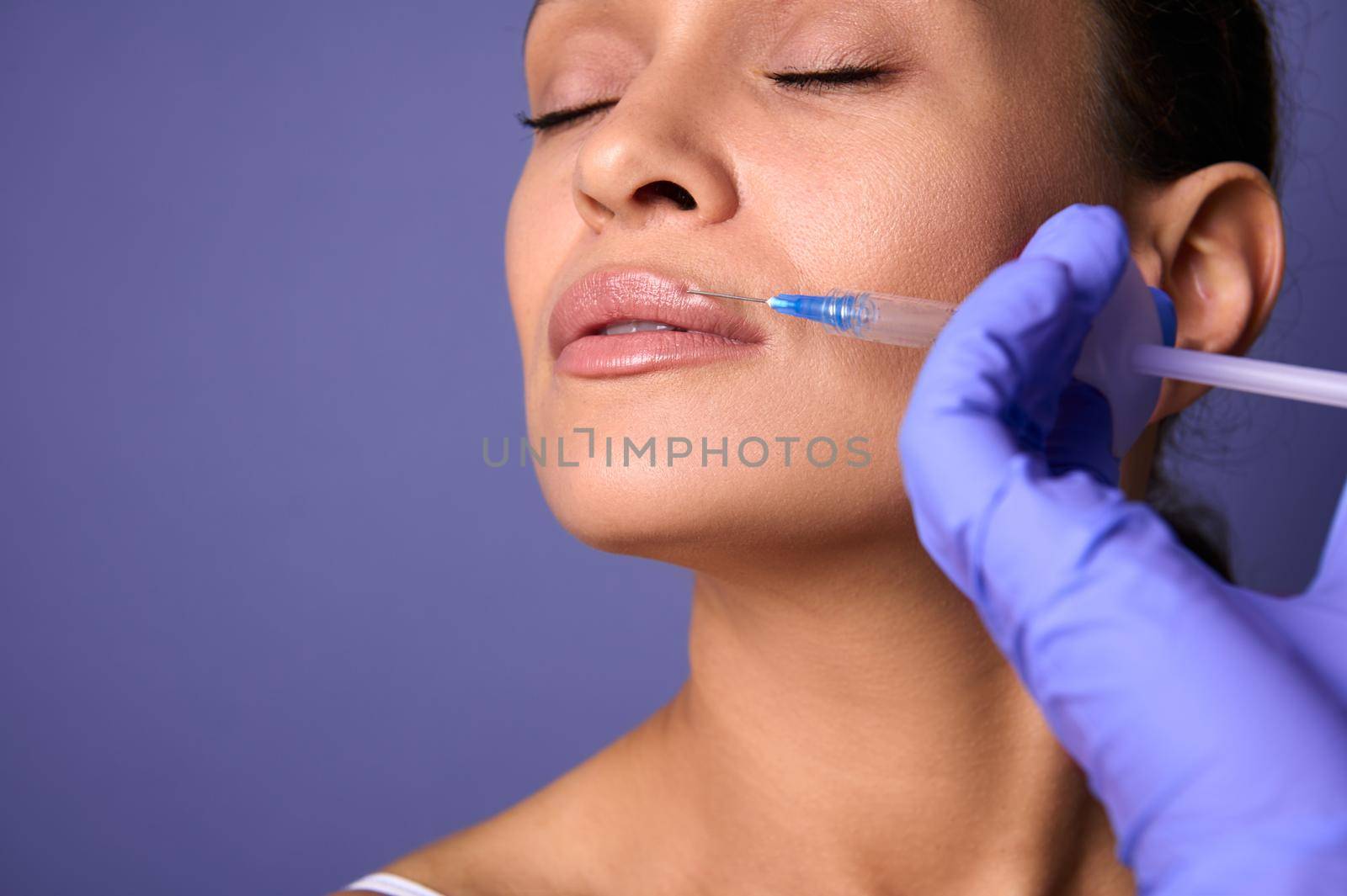 Close-up. Dark-haired charming natural beauty woman with perfect clean healthy skin receiving beauty injection on her lips. Lips augmentation and correction concept. Aesthetic cosmetology and surgery