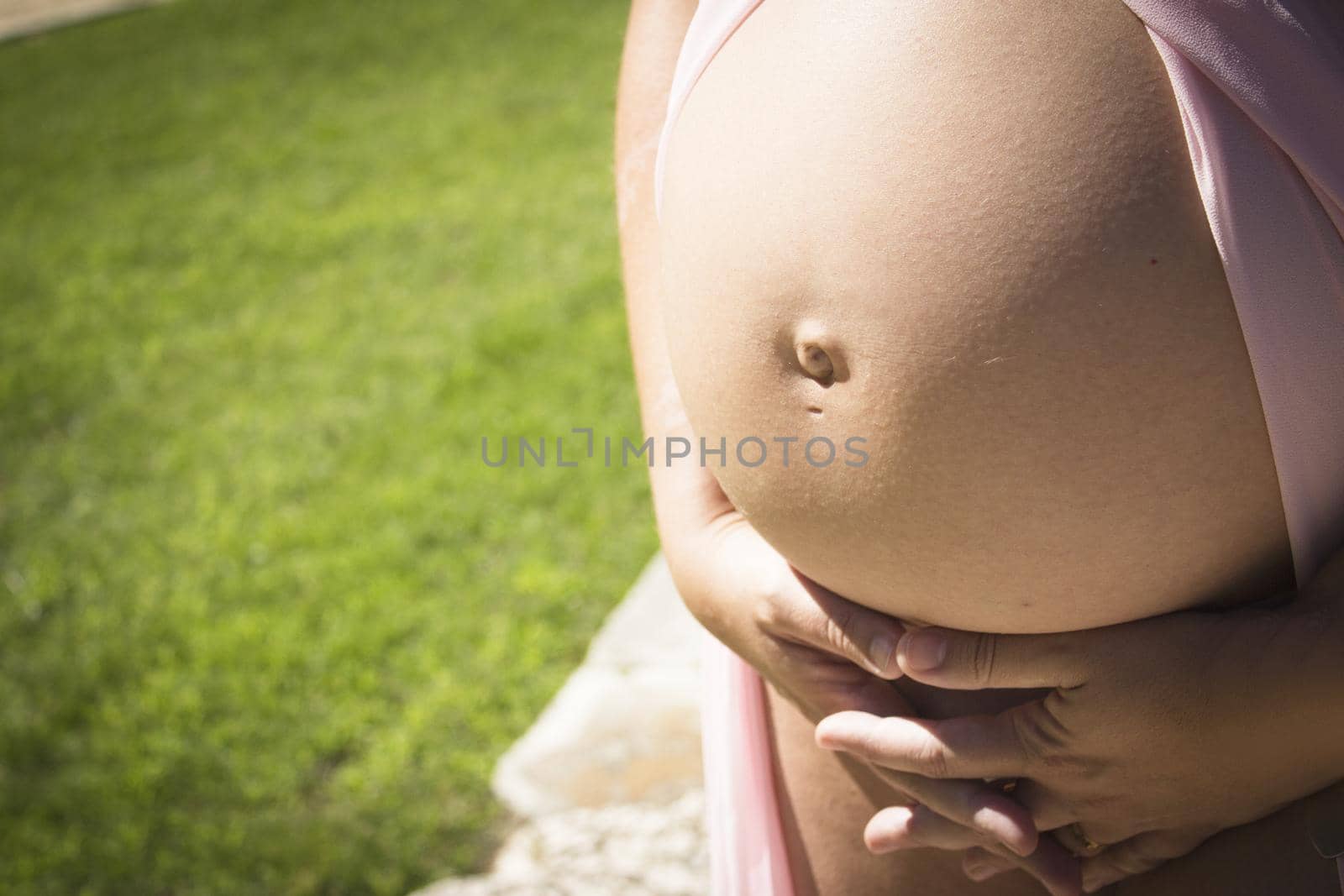 Seven month pregnant woman in pink transparent dress holding belly. Natural background
