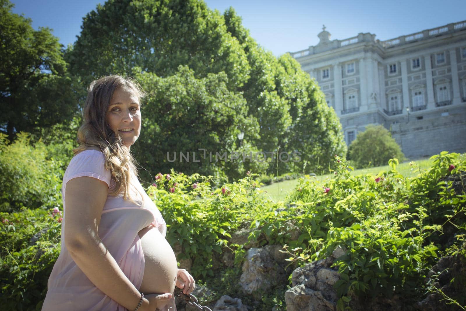 Pregnant woman with pink dress in a park. Sunny day