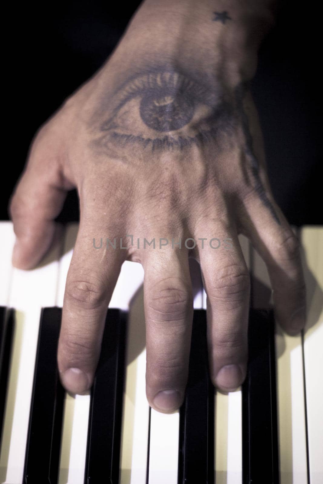 Tattooed mans hands on the keyboard of a piano. Dark background