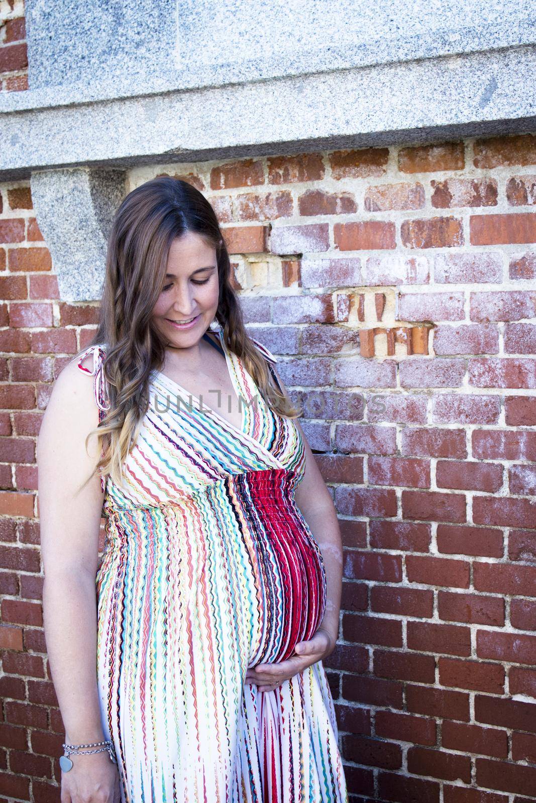 Seven month pregnant woman outdoors in multi colored striped dress. Day scene