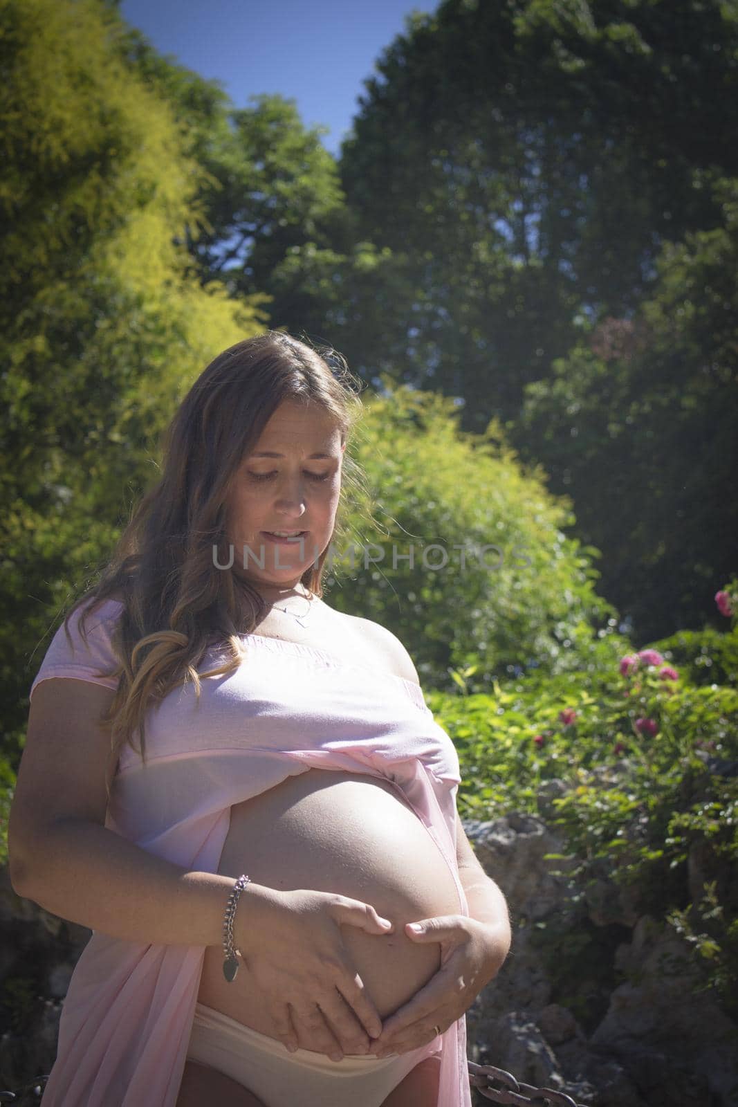 Pregnant woman with pink dress in a park. Sunny day