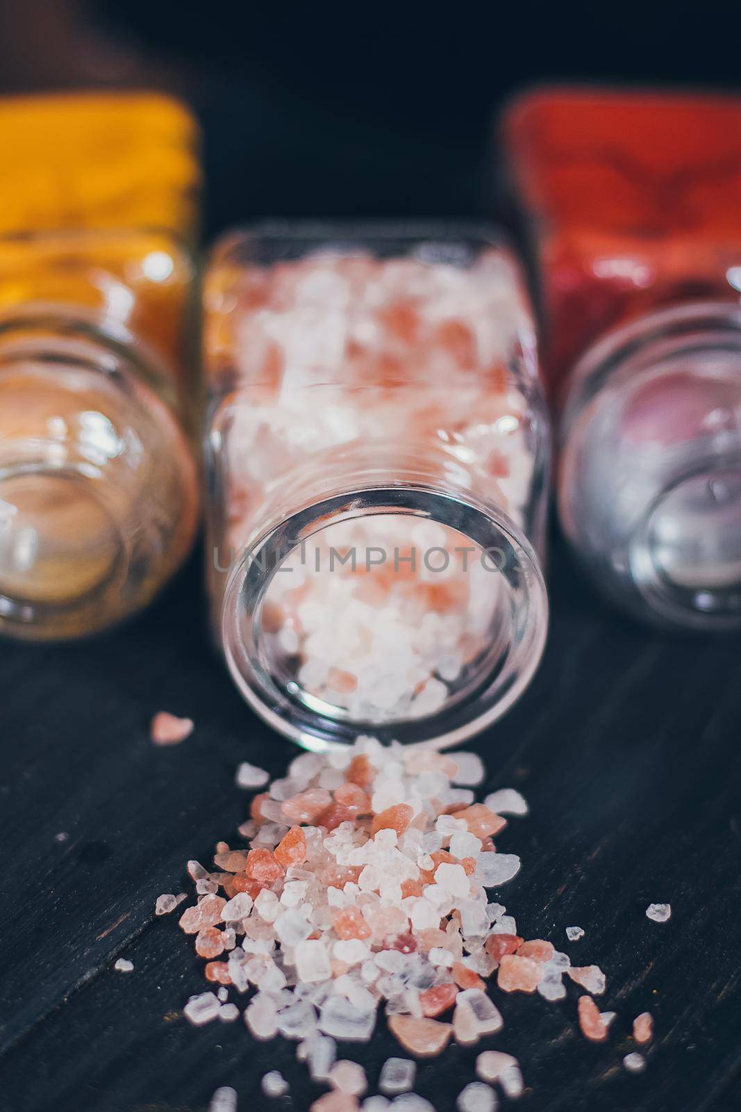Bright aromatic spices in glass jars, assortments of spices: pink salt, paprika and turmeric on black stone background. by mmp1206