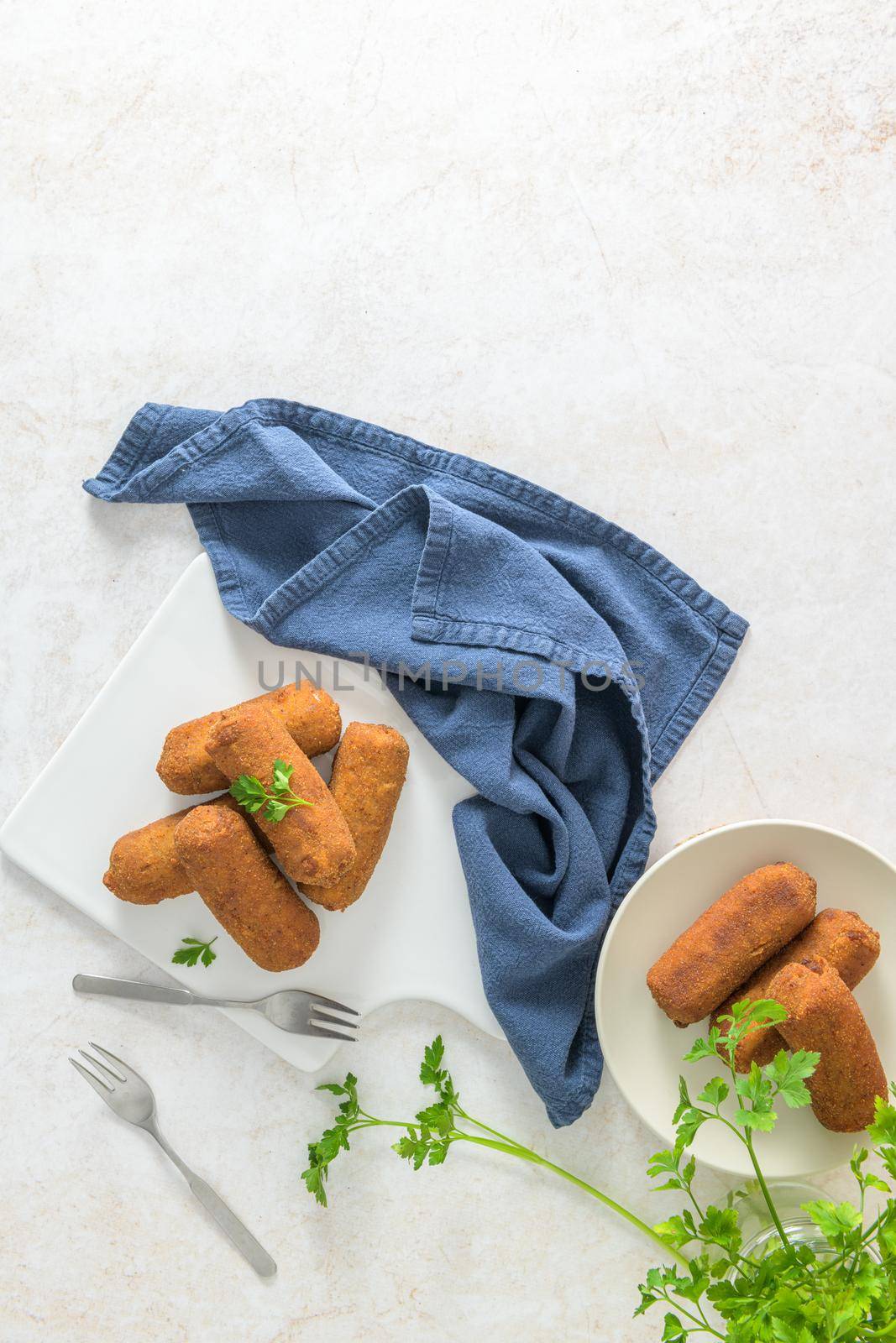 Meat croquets and parsley leaves on white ceramic dishes in a kitchen counter top.