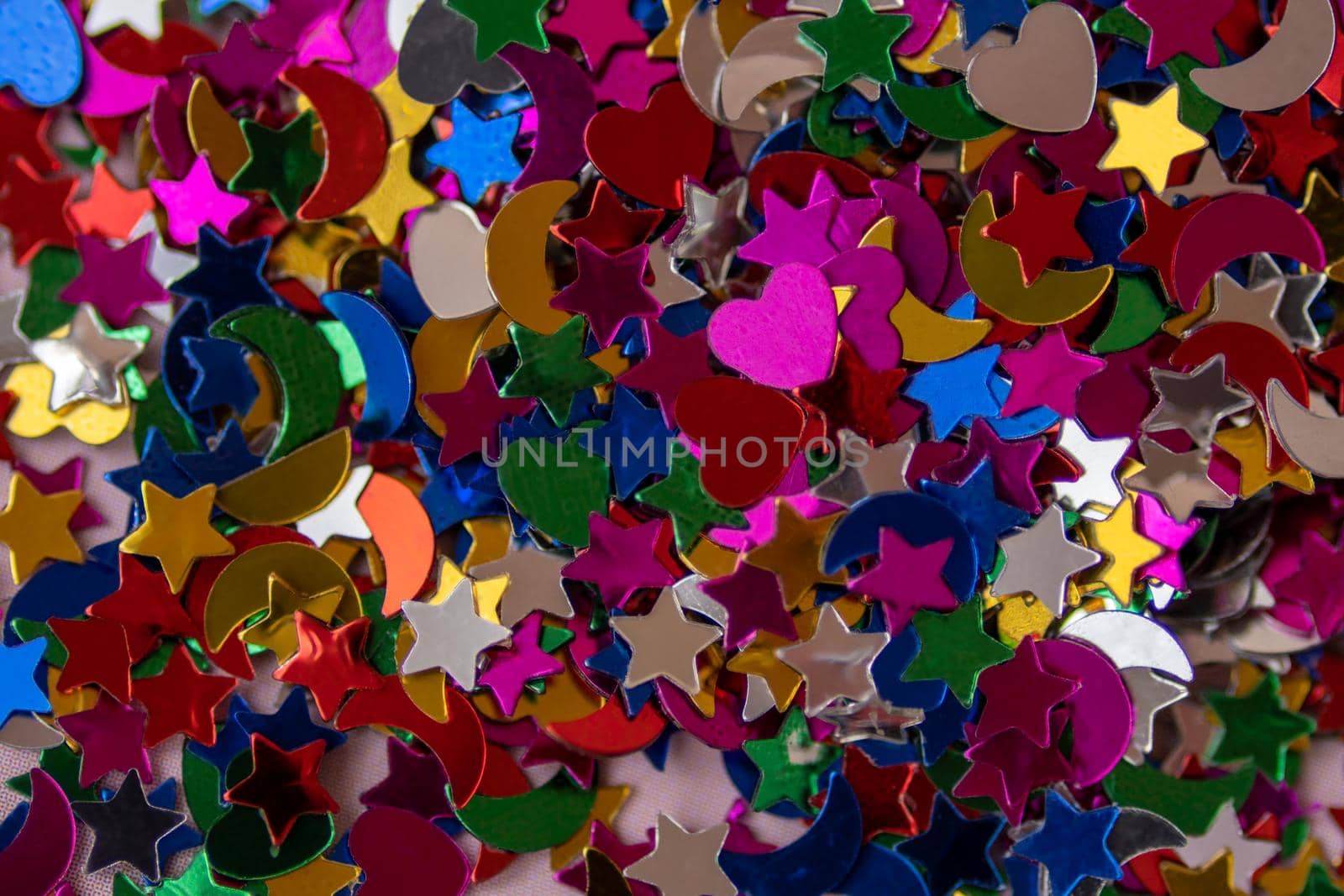 Pink, violet, yellow, green, blue, red stars, hearts, and moons confetti and glitter in macro. Abstract festive background. Light trendy silver shimmering parts for bright presentation color 2022