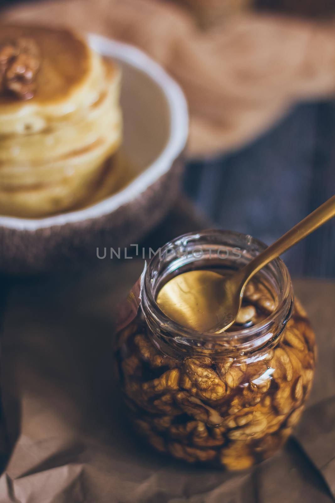 A glass jar of honey with nuts on wooden background.