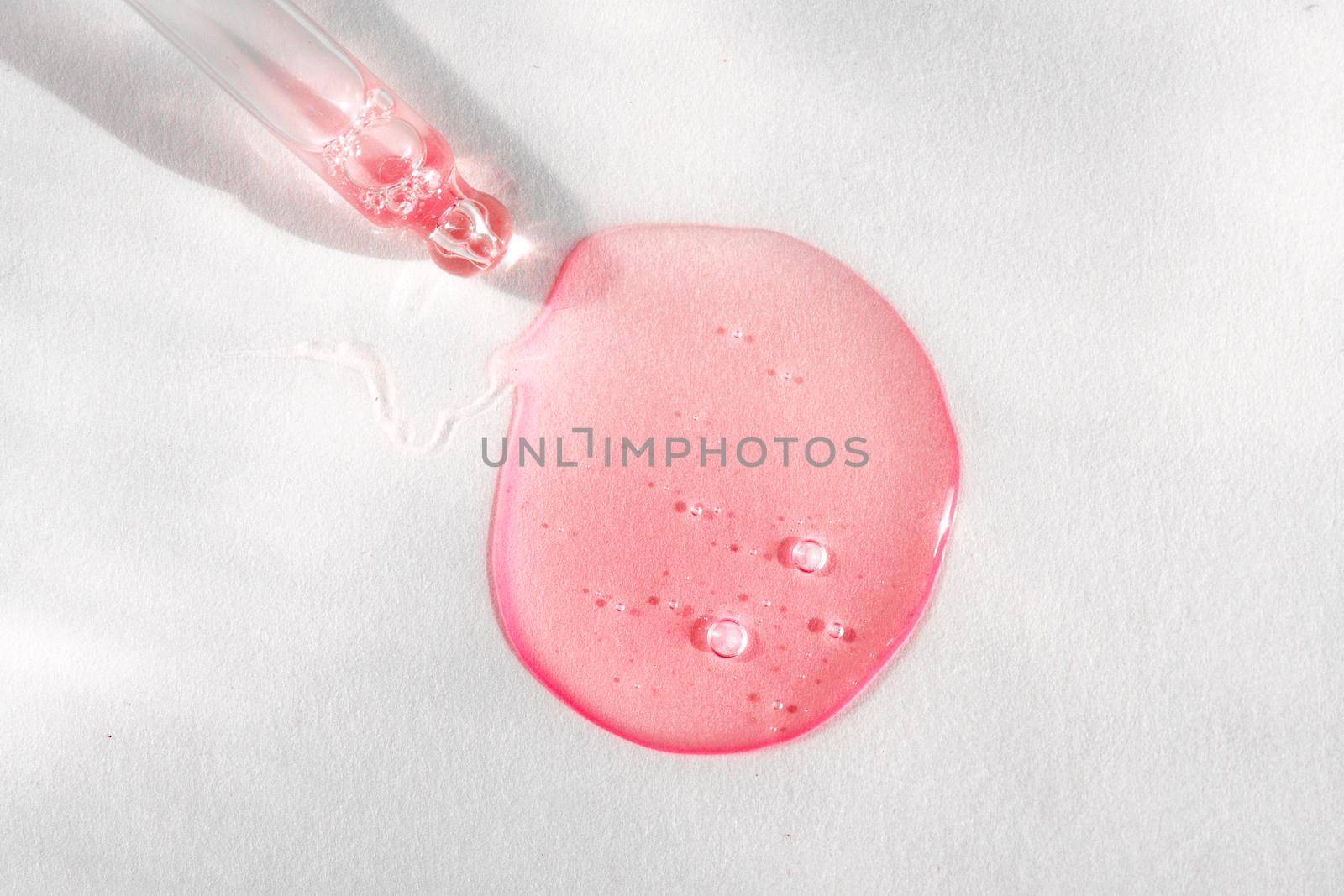Pipette with pink fluid hyaluronic acid on white background. Cosmetics and healthcare concept. Dose of serum or retinol with air bubbles. Flatlay. Luxury gel or beauty product presentation in macro