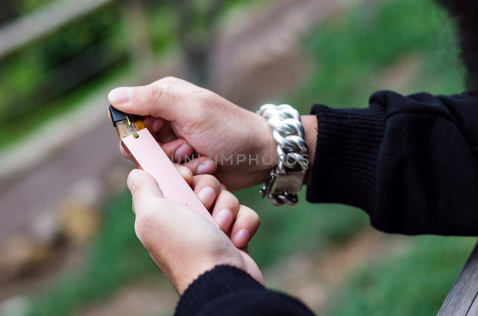 Close-up of person hand holding electronic cigarette, with green background and a silver watch in his hand