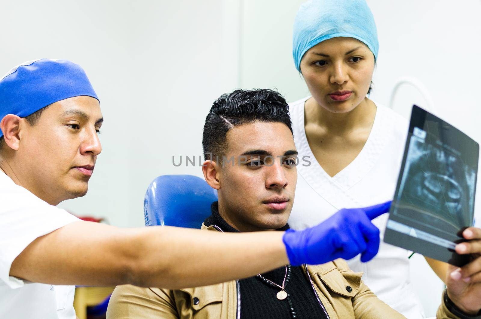 Dentist with nurse showing patient his teeth x-ray. by Peruphotoart