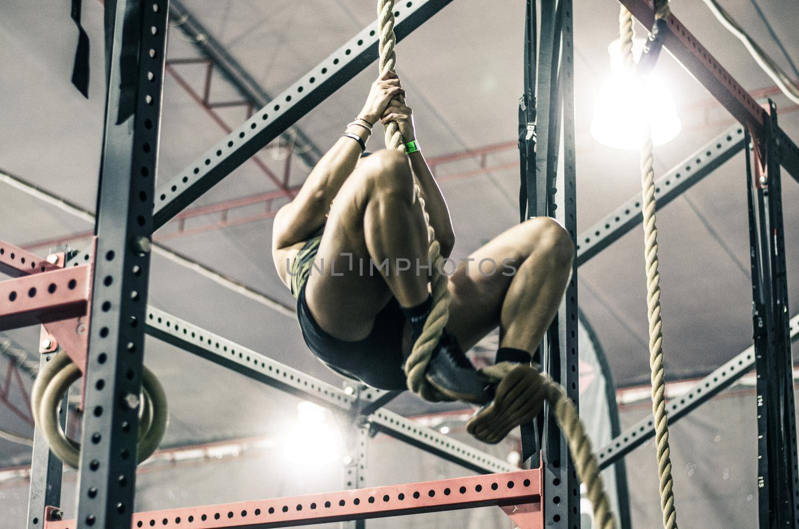 Unrecognizable young athletic woman working and climbing a rope in a gym