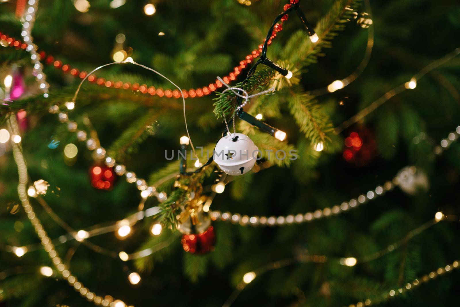 Small white ball-bell on the branches of a Christmas tree in garland lights. High quality photo