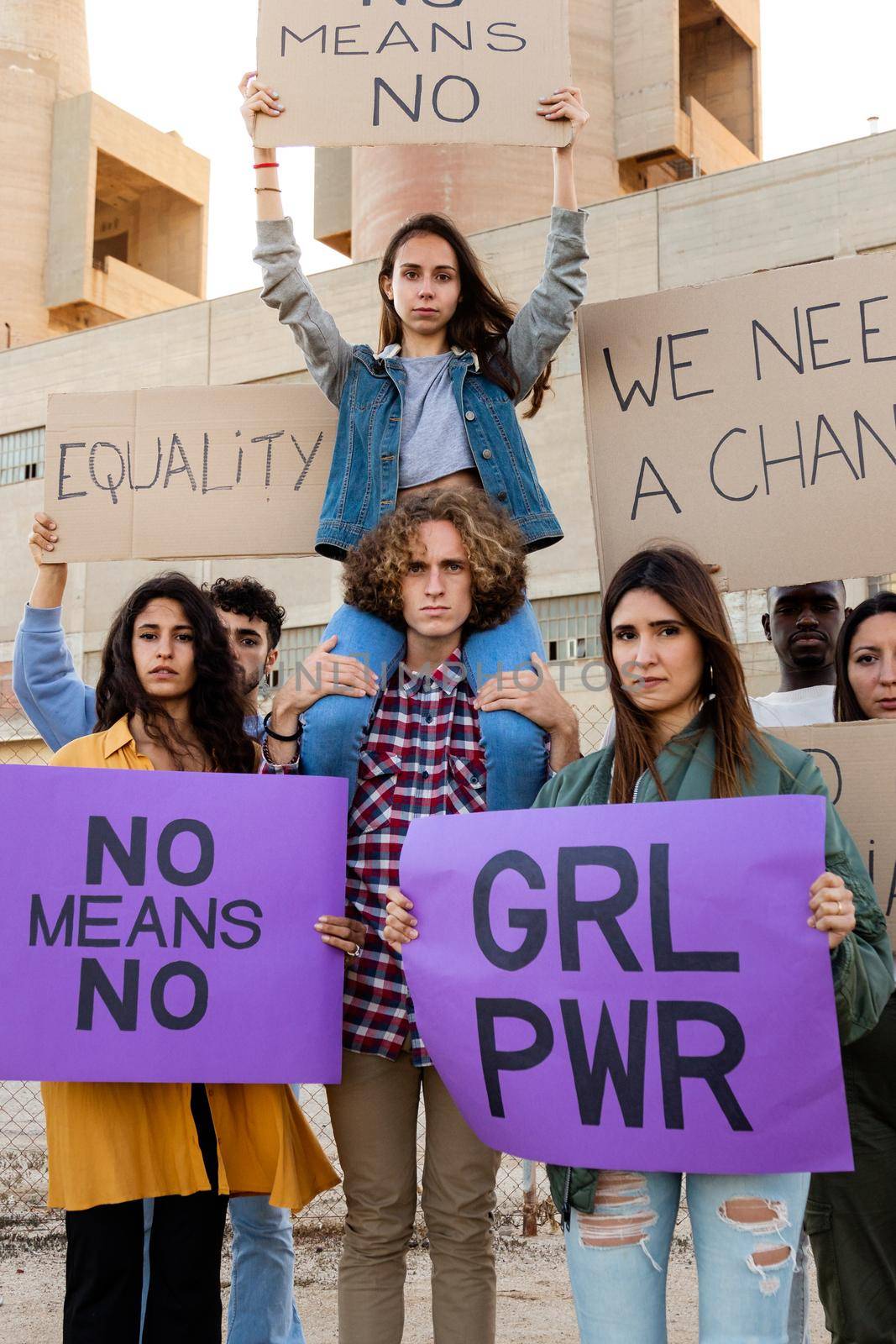 Young female protester sitting on man's shoulders holding a no means no signs in the middle of demonstration. Vertical image. Equality and woman's rights concept.