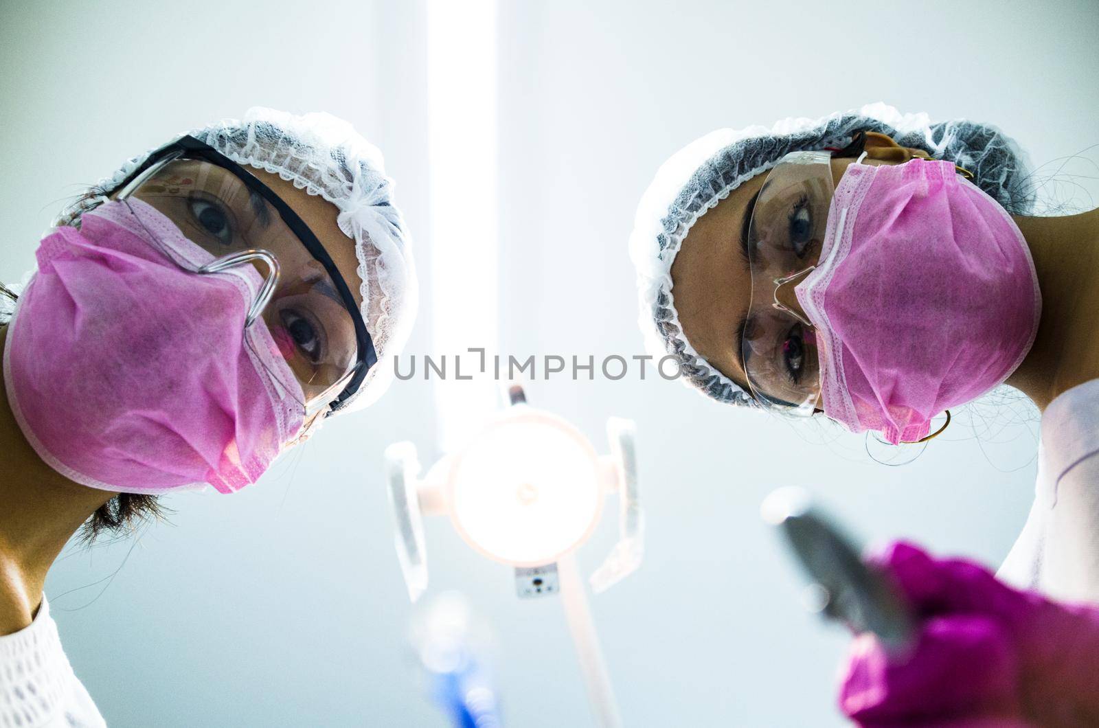 Bottom view of two women dentists in surgical mask holding tools and looking at camera by Peruphotoart