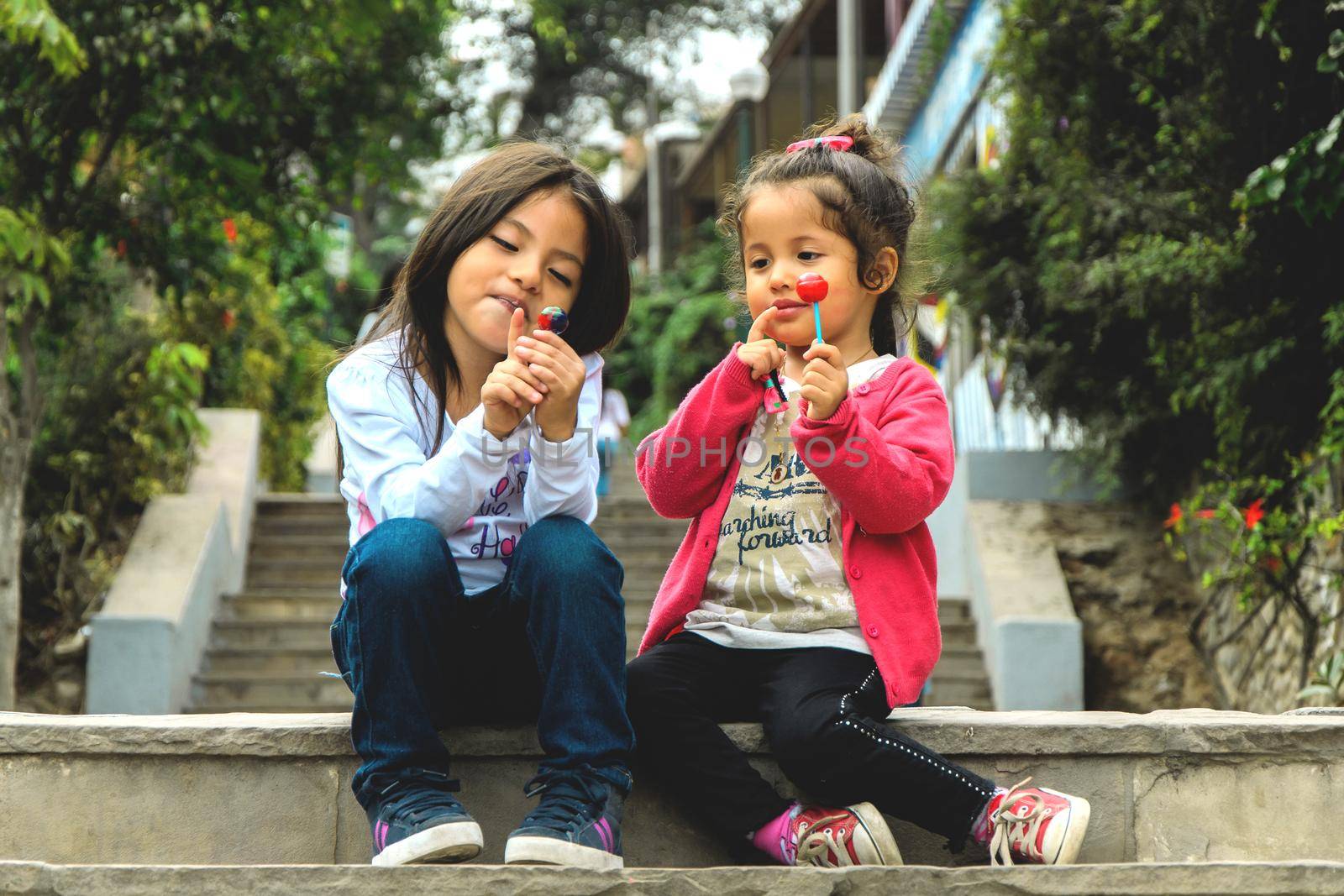 Two girls sitting and eating a lollipop in the park, summer outdoor portrait. best friends