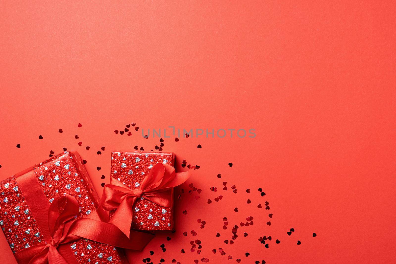 Valentines Day. Red Gift boxes with beautiful red ribbon with heart shape confetti on red background with copy space