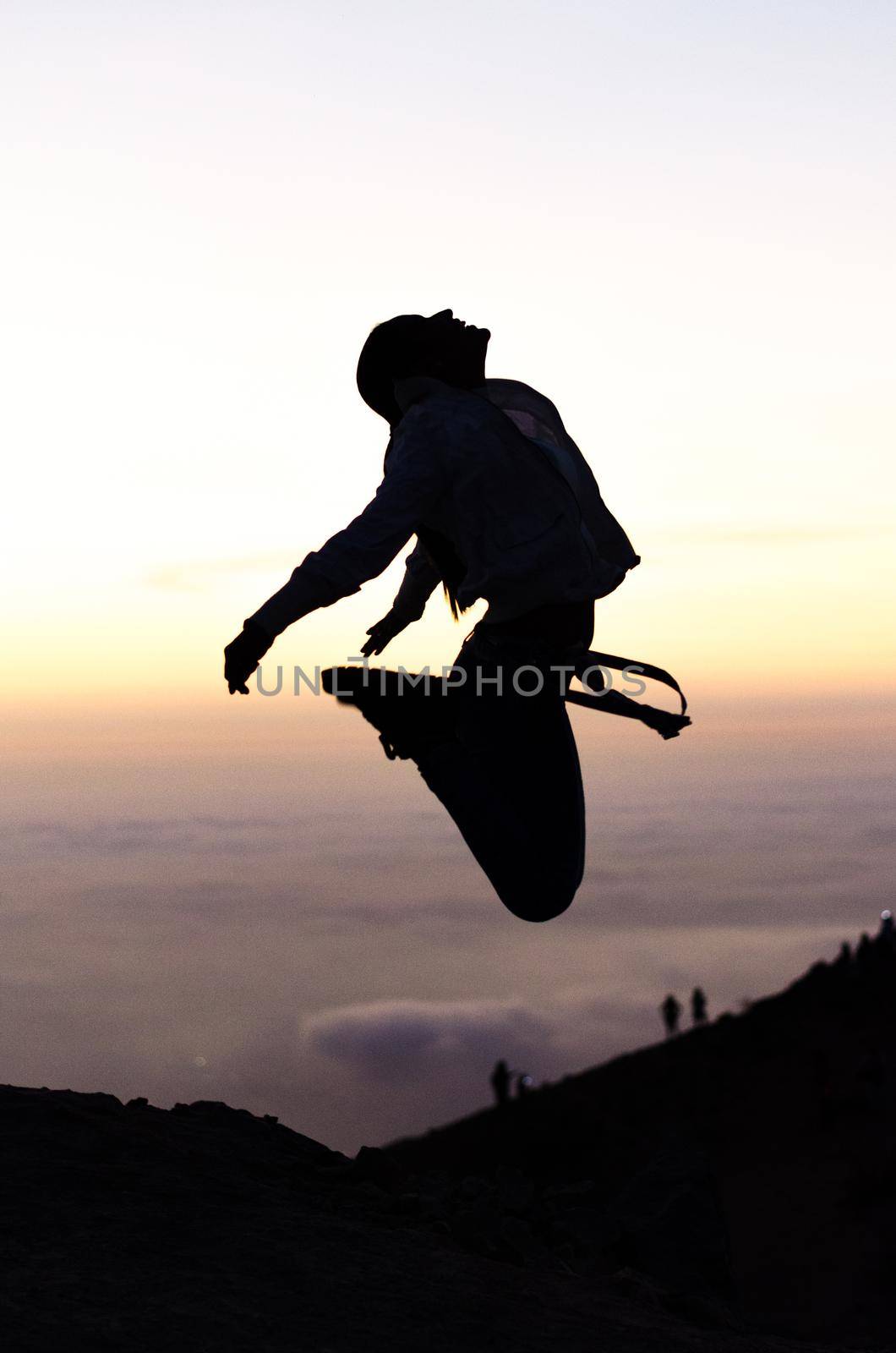 Silhouette of a beautiful jumping woman against yellow sky with clouds at sunset in Apu Siqay in Lima - Peru