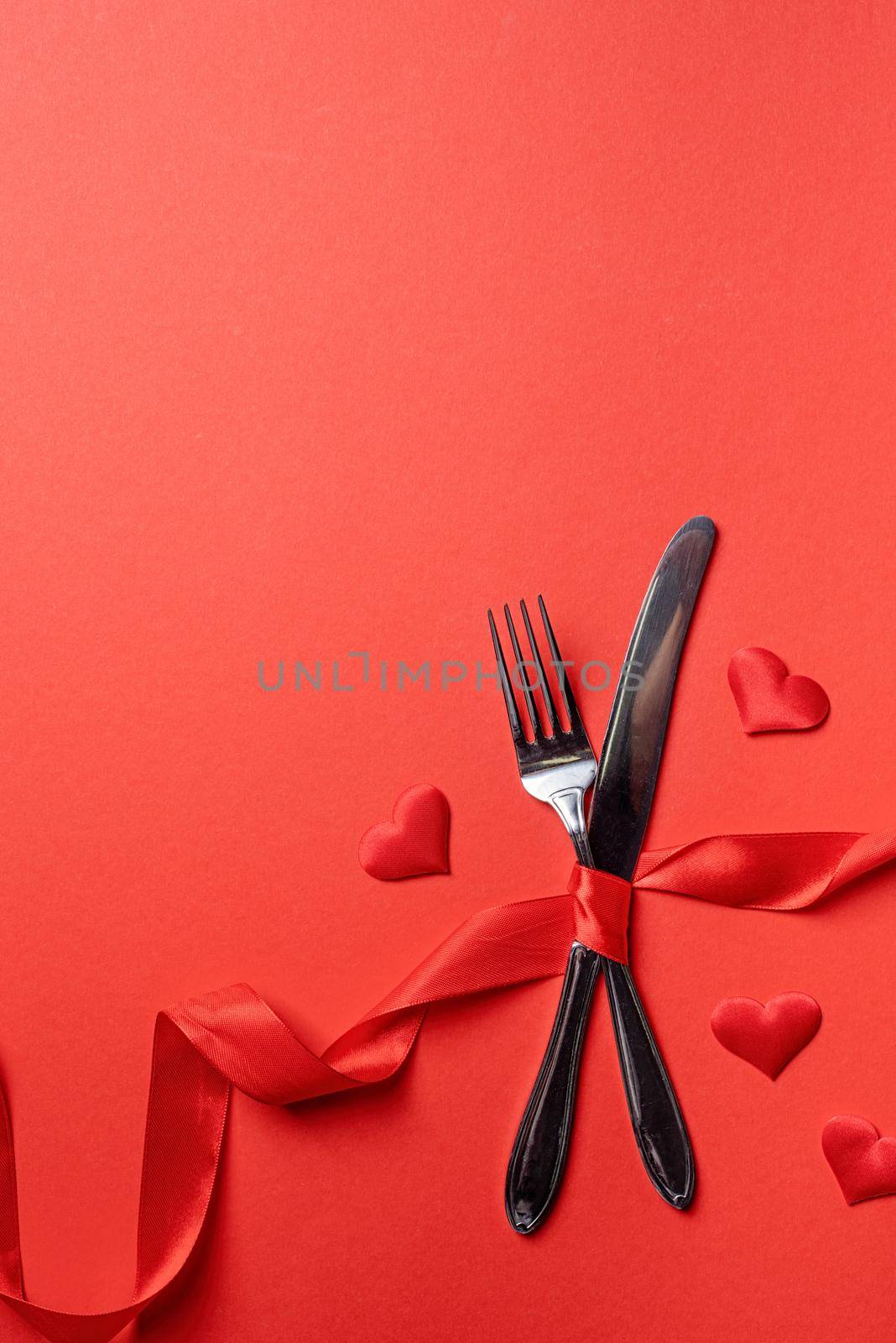 Fork and knife tied with a red ribbon in a shape of heart rate on red background by Desperada