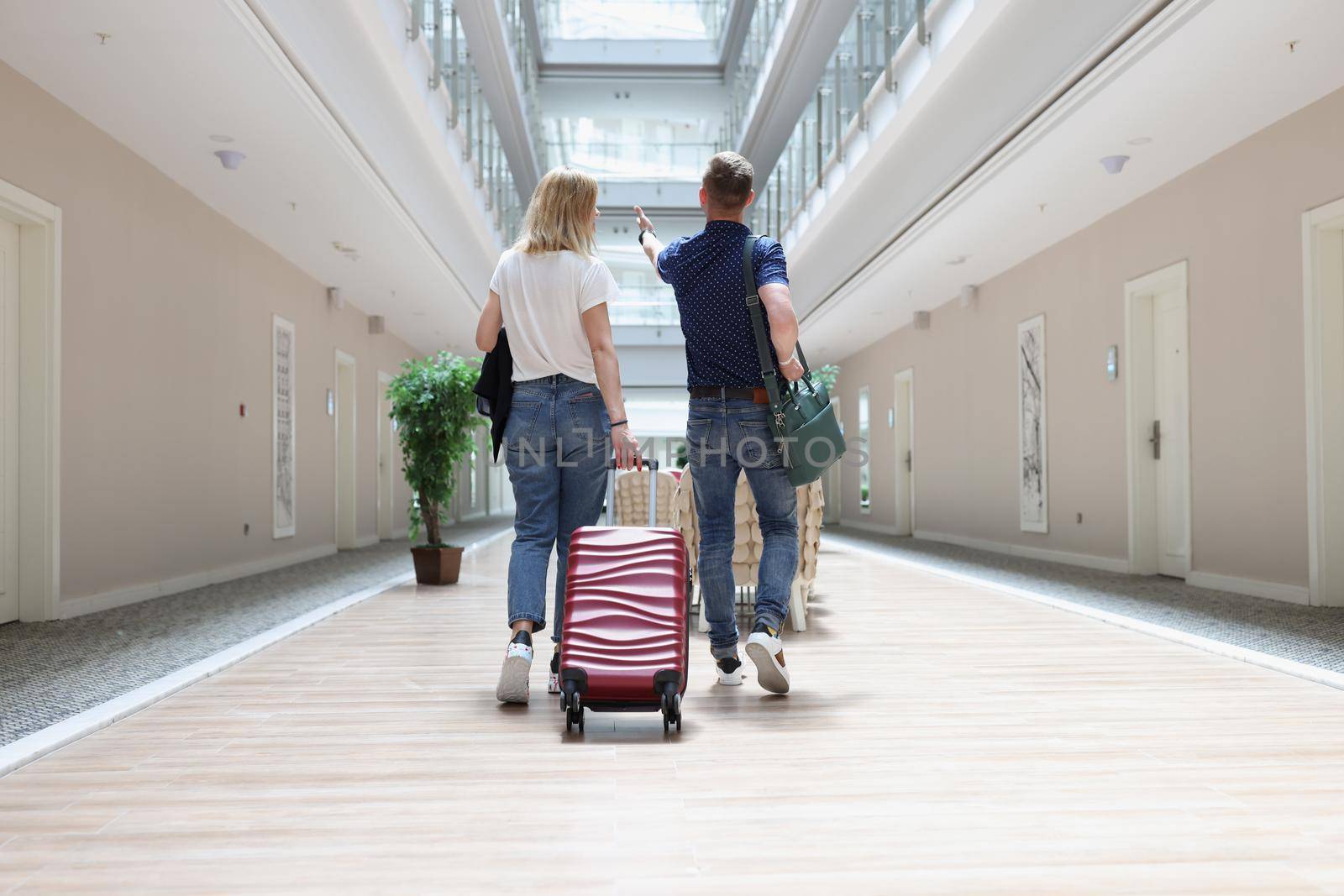 A man and a woman are walking with luggage along the hotel corridor, close-up, rear view. Accommodation in a resort complex