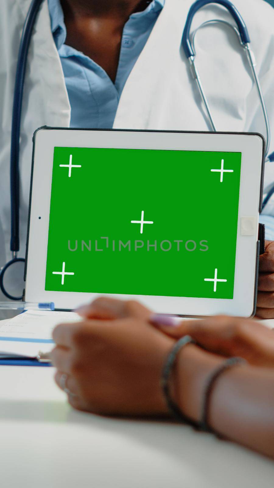 Close up of horizontal green screen on digital tablet at checkup visit. Doctor pointing at mockup template with chroma key and isolated background to show technology to patient.