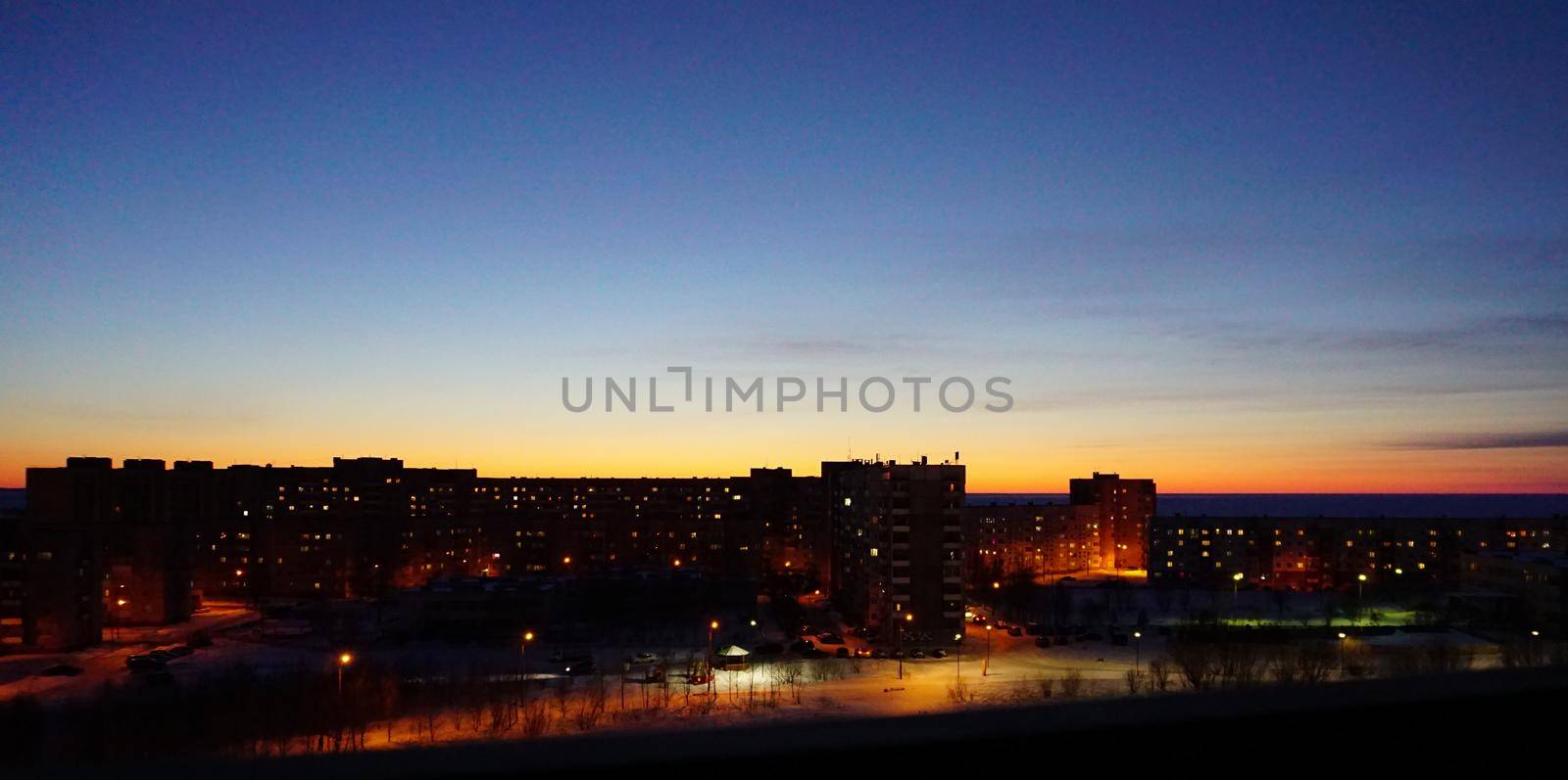 SEVERODVINSK, RUSSIA - MARCH, 11, 2021: Bright winter sunset against the background of houses. Multi-story houses in the rays of the sun. The sun goes down behind the houses