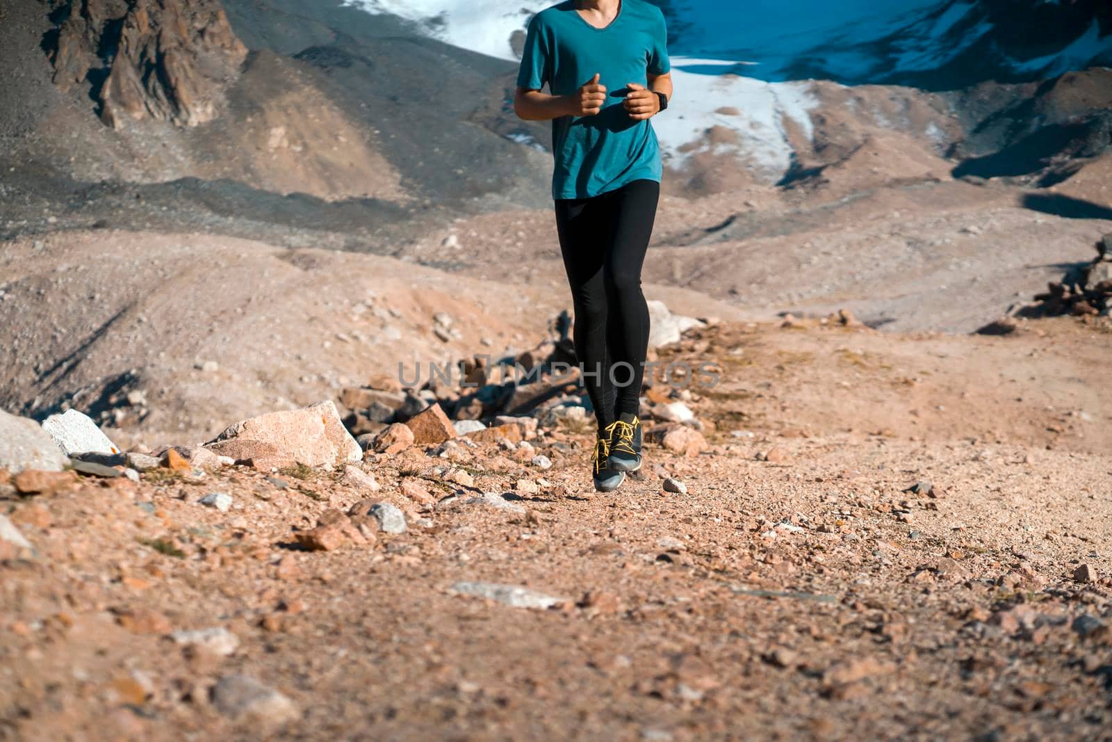 A young man runs along a trail in the snow-capped mountains, doing outdoor workout. The runner warms up, prepares for the race, leads a healthy active lifestyle.