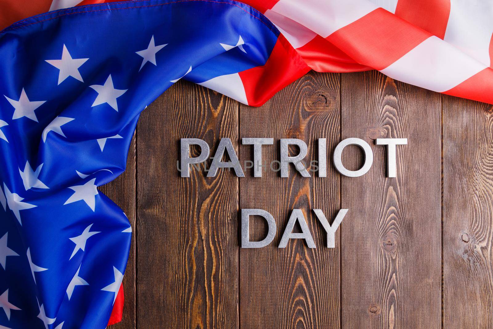 the words patriot day laid with silver metal letters on wooden board surface with crumpled usa flag above and left side, in flat lay high angle directly above view