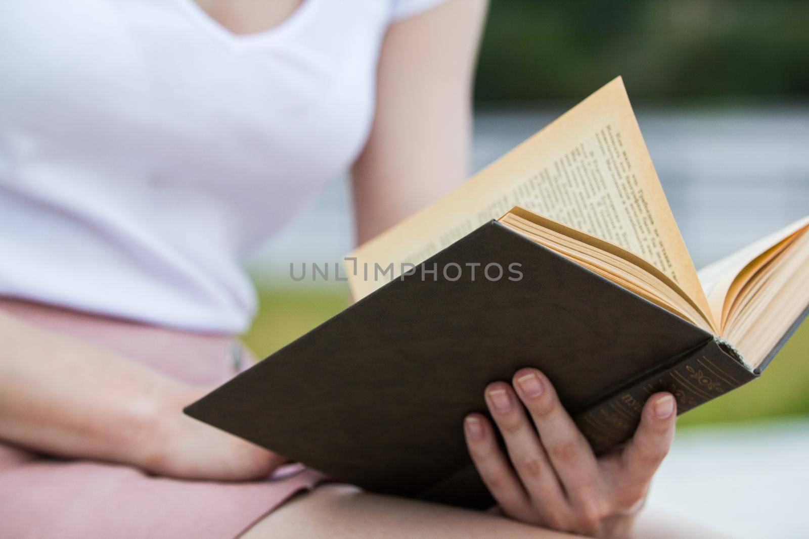 Young woman holding an old book in her hands outdoors, close up