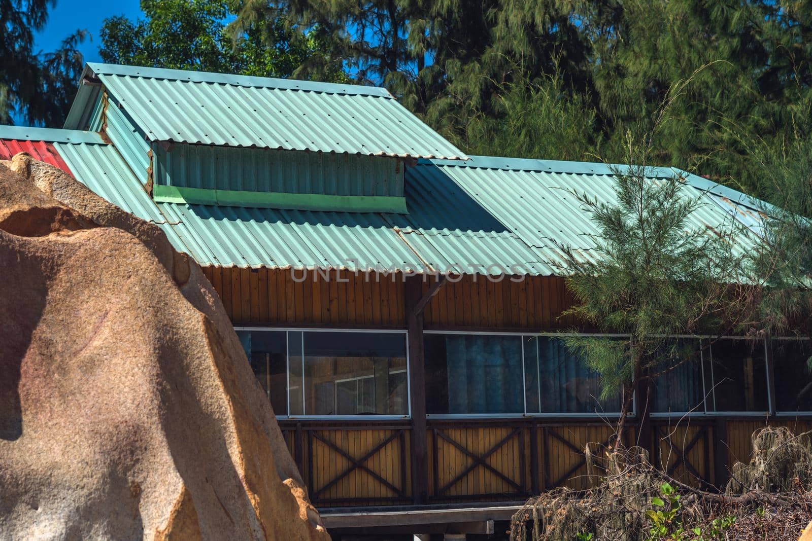 Outside view facade. Wood yellow boards material country house, panoramic window glass metal roof tiles. Summer day warm light mood nature forest Cozy home exterior eco building. Huge stone landscape