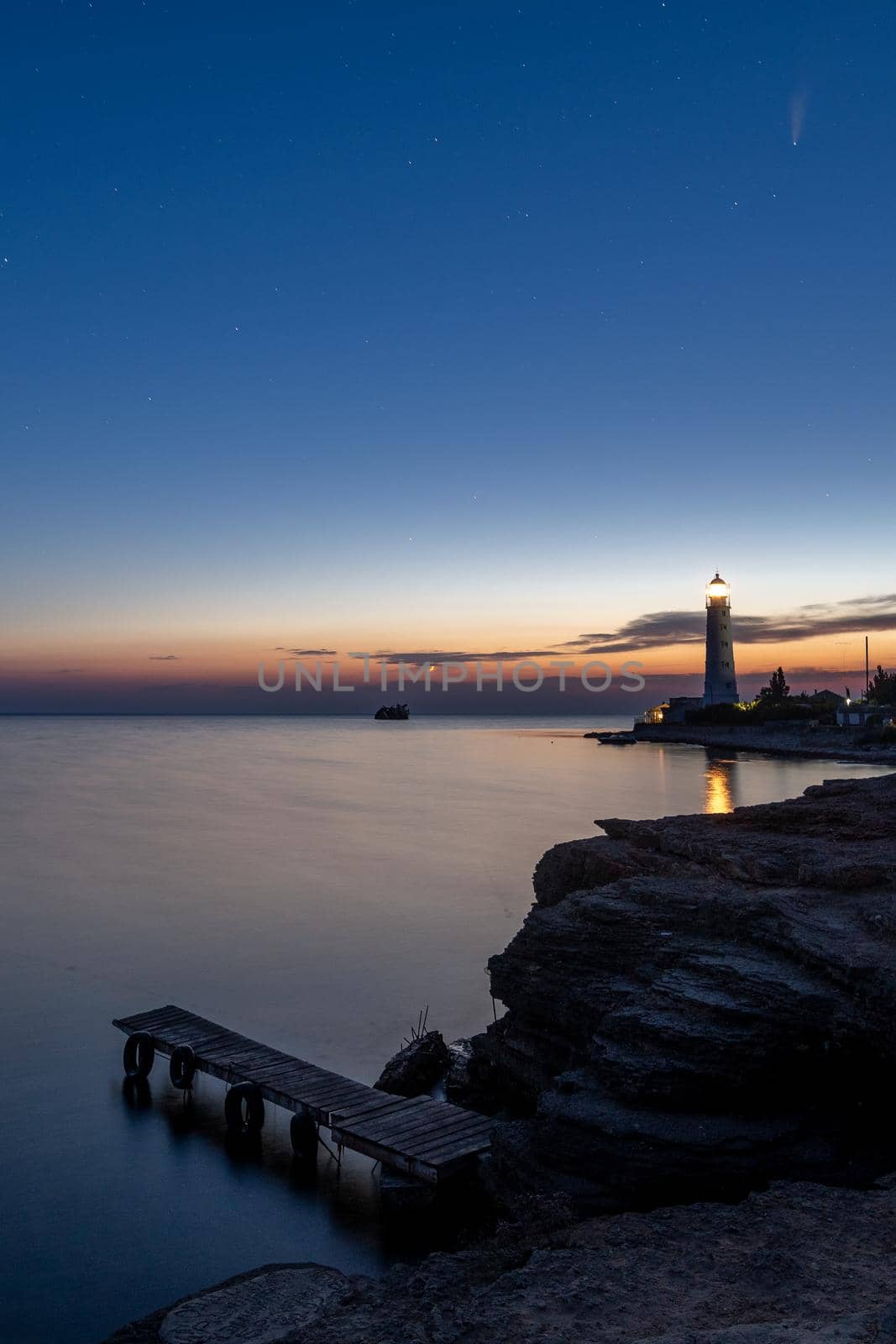 Panoramic HDR Landscape view of Neowise comet over white Lighthouse at night sky. High quality photo