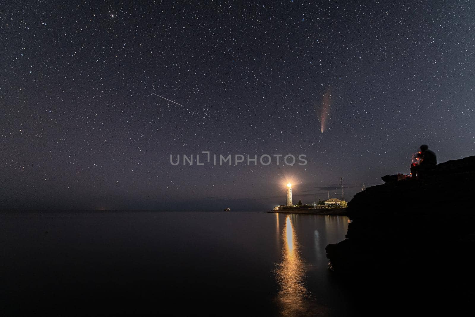 Person smoking and looking at Neowise comet over white Lighthouse at night sky by MKolesnikov