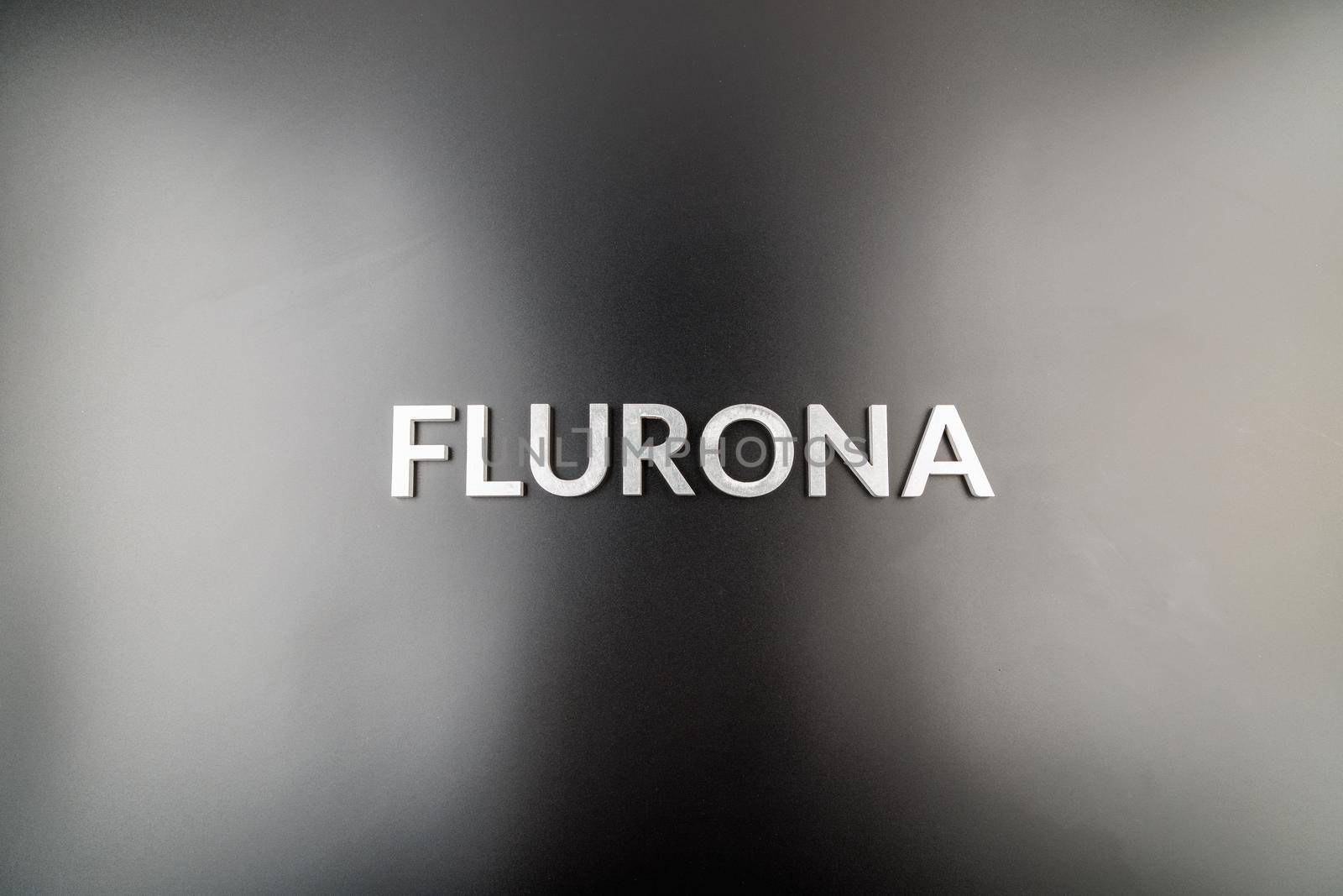 the word flurona laid with silver metal letters on gloss black background, real life photo for flu plus covid concept in high angle flat lay view