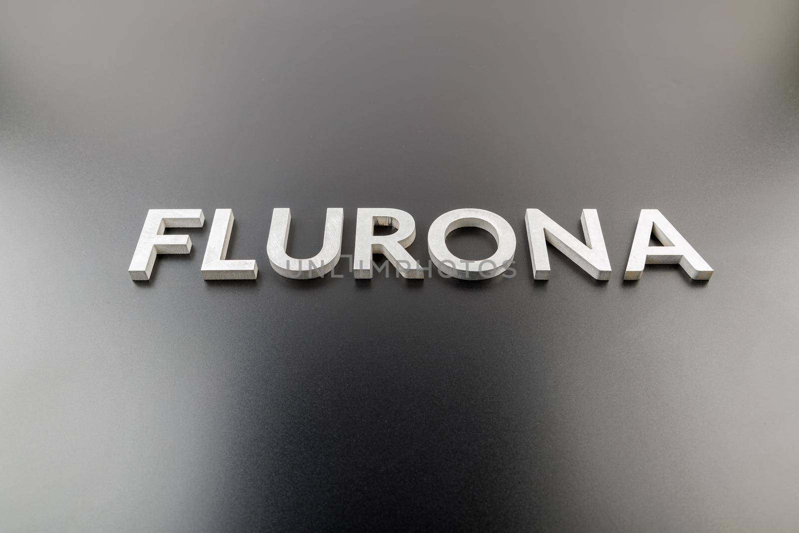 the word flurona laid with silver metal letters on gloss black background, real life photo for flu plus covid concept in frontal perspective view