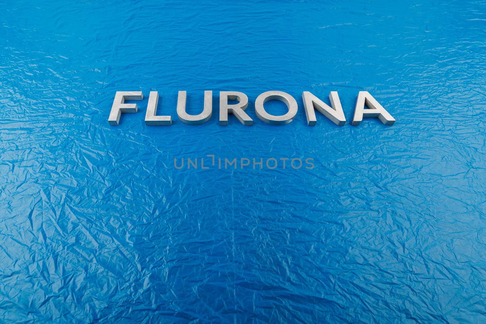 the word flurona laid with silver metal letters on blue crumpled plastic film background, real life photo for flu plus covid concept in frontal perspective view
