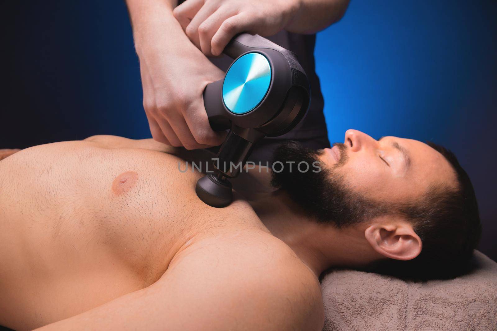 Close-up of a Caucasian male pectoral muscle percussion massager working out in a professional massage parlor.