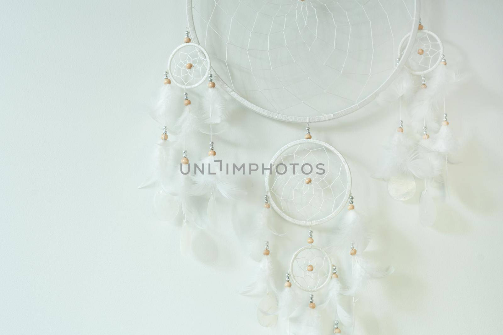 White dreamcatcher hanging on white wall background. handmade willow hoop woven net decorated with feathers. protective charm for infants